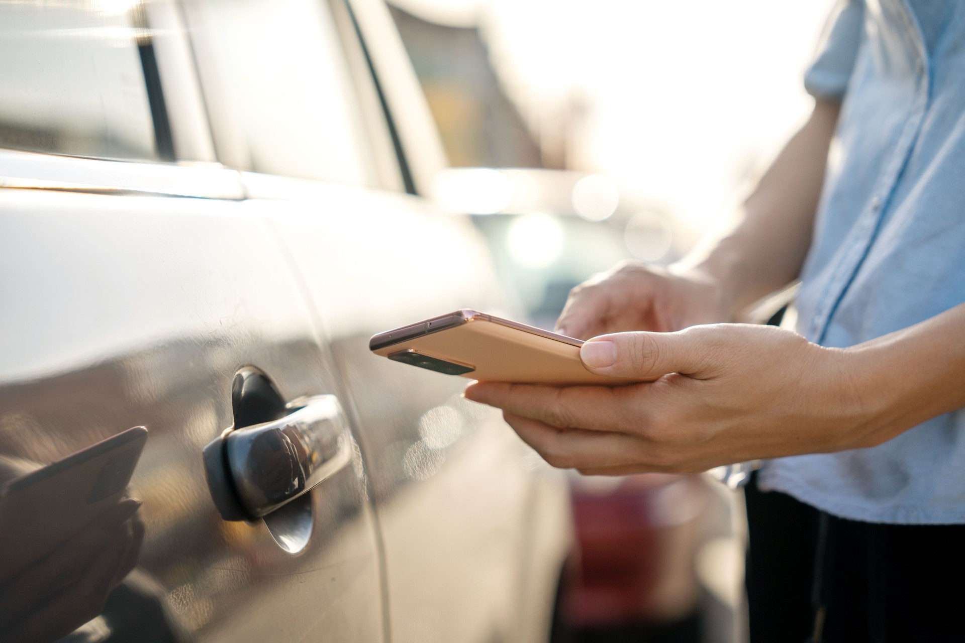 A close-up image of a woman is using a mobile app on her smartphone to remotely unlock the doors of a car. This technology provides a convenient and secure way to access the vehicle, enhancing the user's experience.